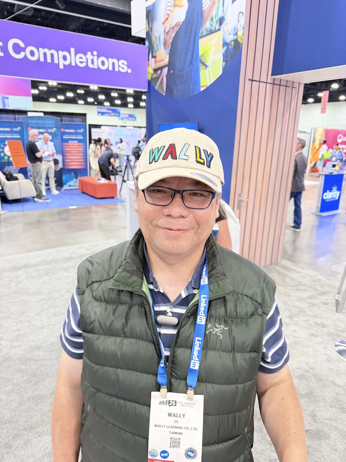 Conference guest wearing a tan cap with multicolor chenille varsity letters spelling his name, pressed at a Merch Troop chenille patch bar
