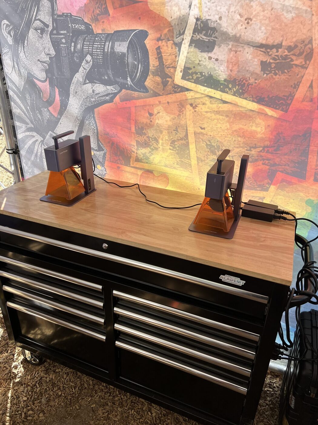 Compact laser engraving units staged on a wood workbench at a Merch Troop event station